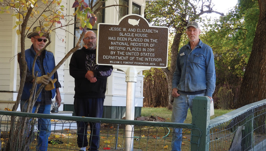 Three men stand in front of the Slagle House, behind a sign they installed